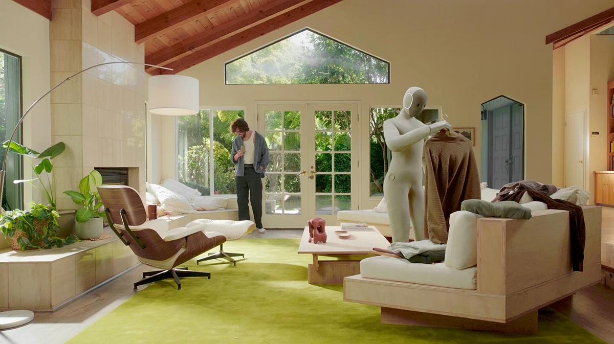 Robot 1X NEO hỗ trợ con người xử lý trang phục trong không gian phòng khách hiện đại.