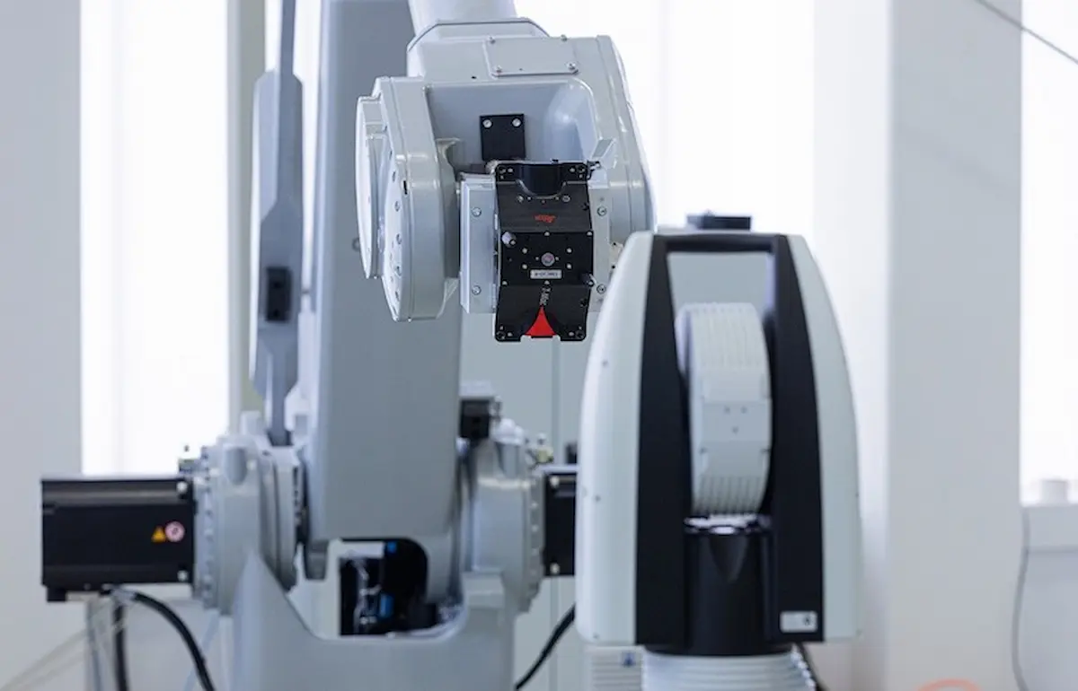 Cận cảnh thiết bị phản xạ gắn trên đầu cuối cánh tay robot đối diện với hệ thống theo dõi laser để ghi nhận sai lệch tọa độ thực tế.