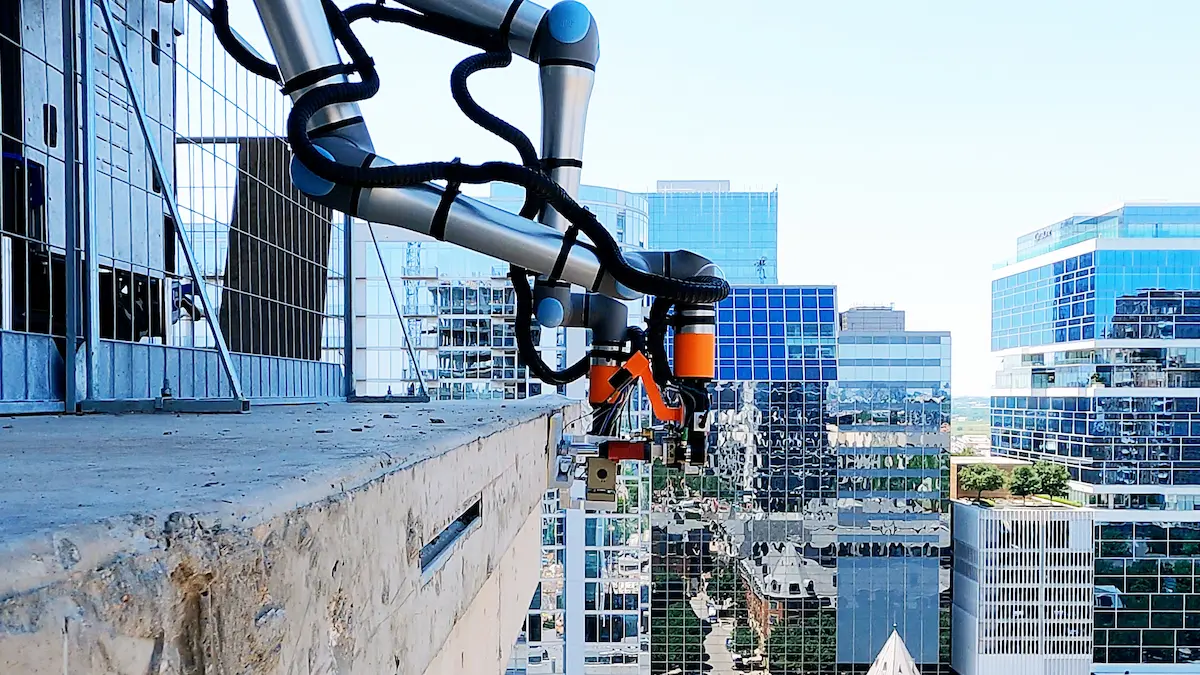 Cận cảnh cánh tay cobot UR20 của Raise Robotics vươn qua mép sàn công trình để lắp đặt neo mặt tiền.