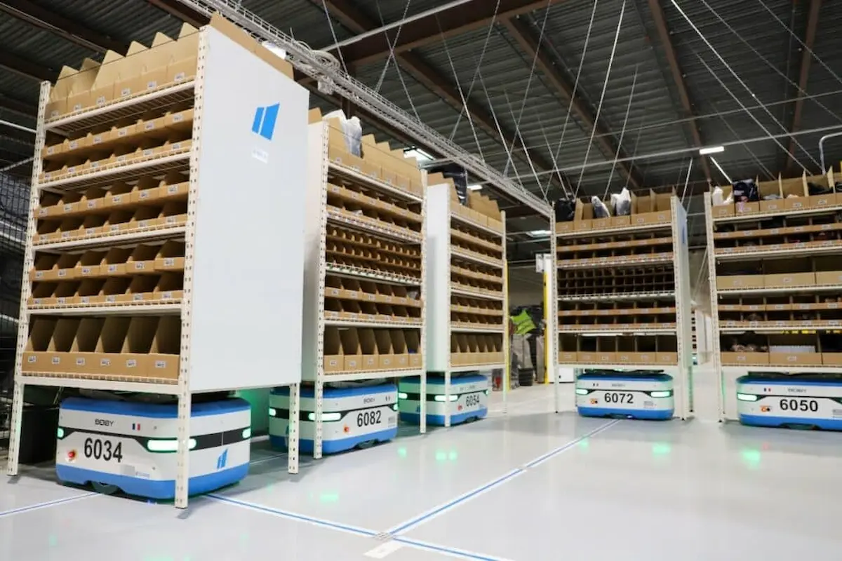 Hạm đội robot Scallog Boby đang vận chuyển các giá kệ di động trên sàn kho kẻ vạch quang học.