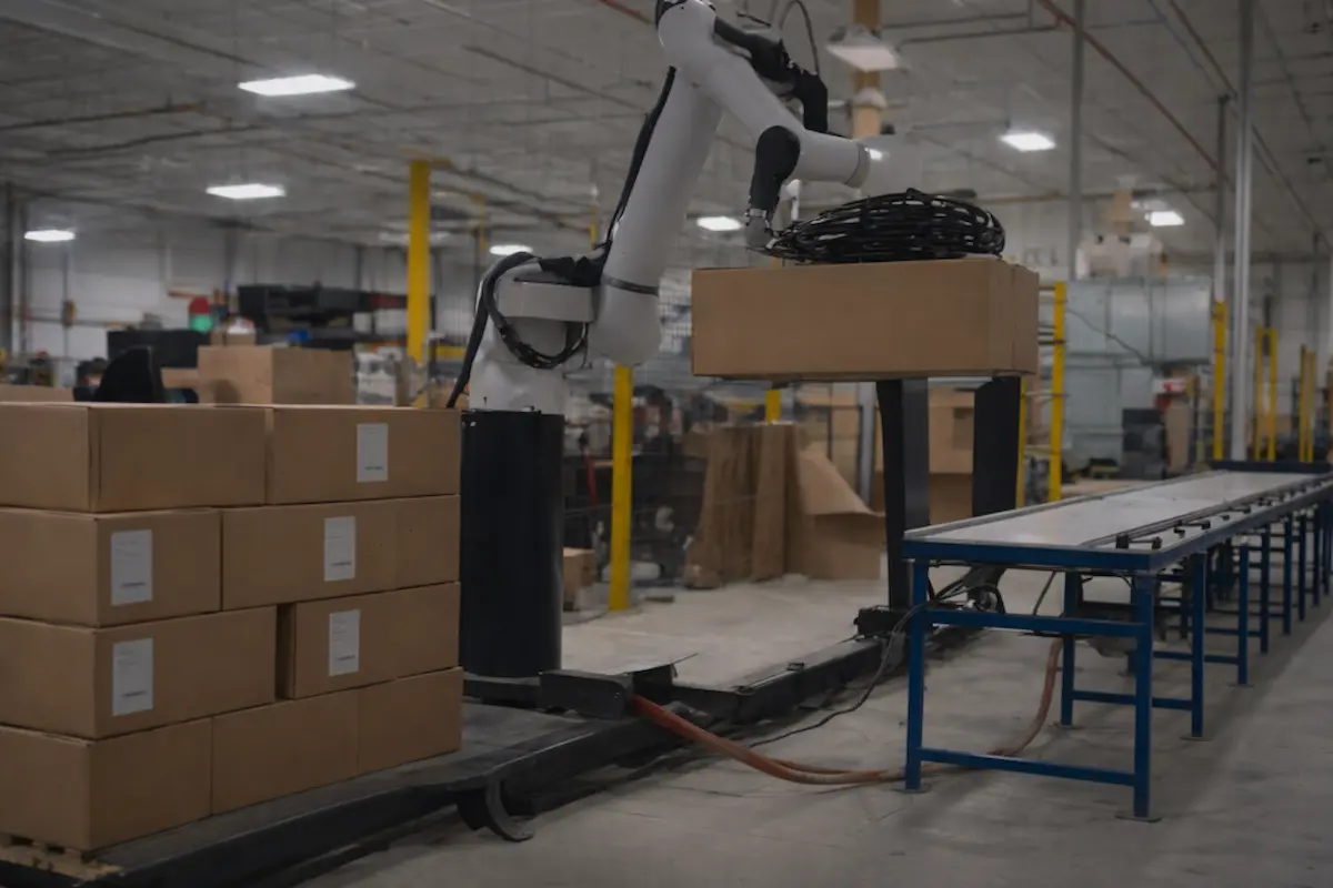 Cánh tay robot bốc xếp (palletizing arm) hoạt động xếp các thùng carton lên pallet trong nhà kho logistics.