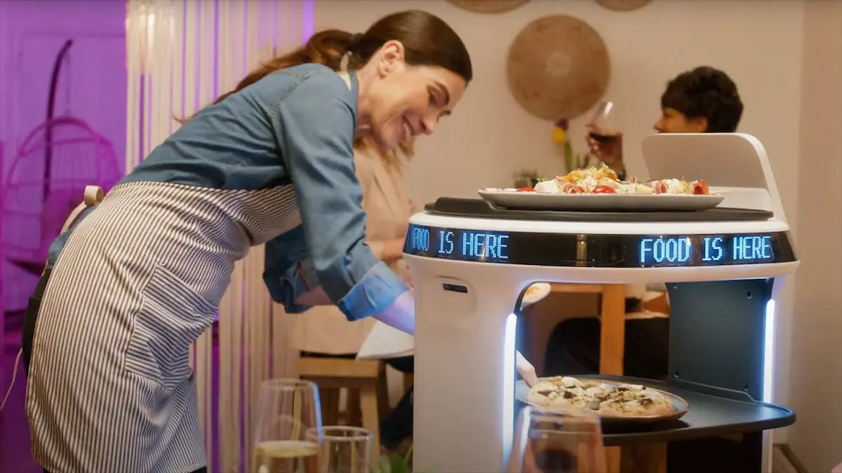 Nhân viên nhà hàng mỉm cười lấy bánh pizza từ Robot Servi Plus mượt mà trong ca làm việc.